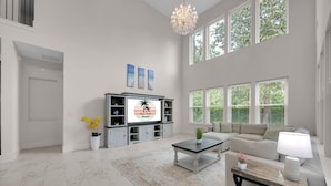 A spacious living room with a large TV, a sofa, a coffee table, and a chandelier. - Salt Air 6BR Game Room Walk to Beach Luxe (Ponte Vedra Beach)