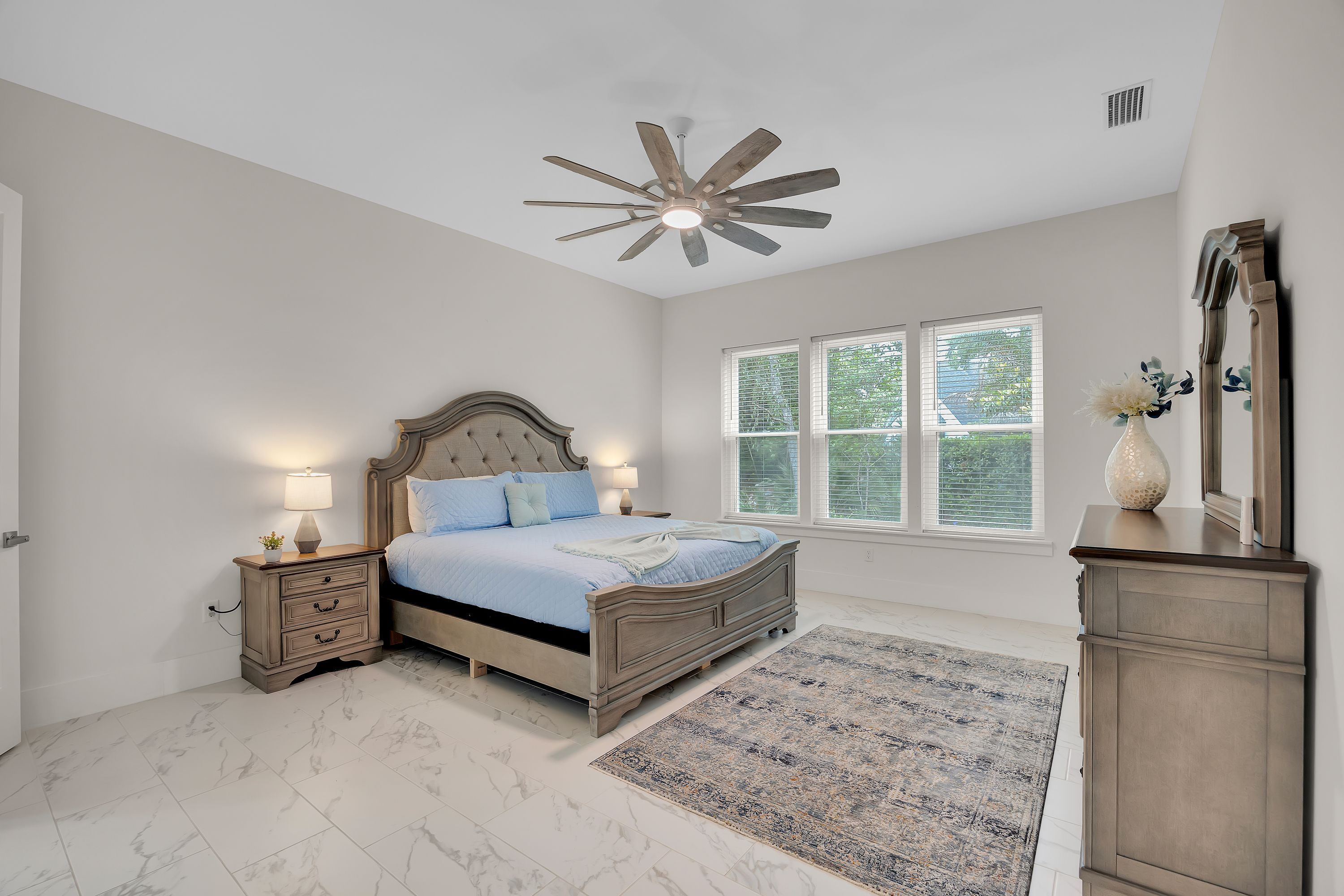 A bedroom with a bed, nightstands, a ceiling fan, a window with blinds, and a mirror.