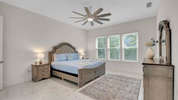 A bedroom with a bed, nightstands, a ceiling fan, a window with blinds, and a mirror.
