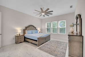 A bedroom with a bed, nightstands, a ceiling fan, a window with blinds, and a mirror.