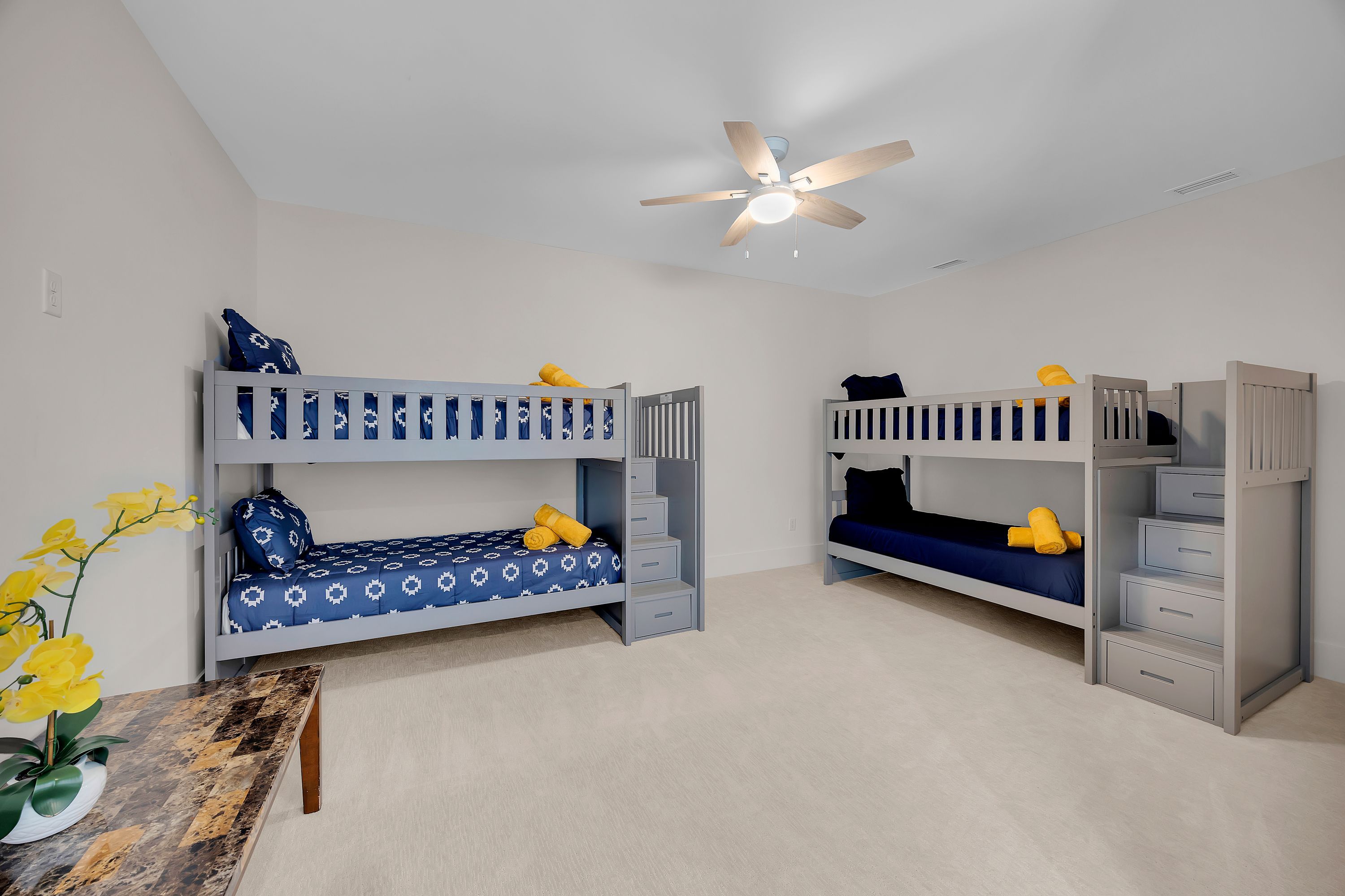 A room with two bunk beds, a ceiling fan, and a small table with a plant.