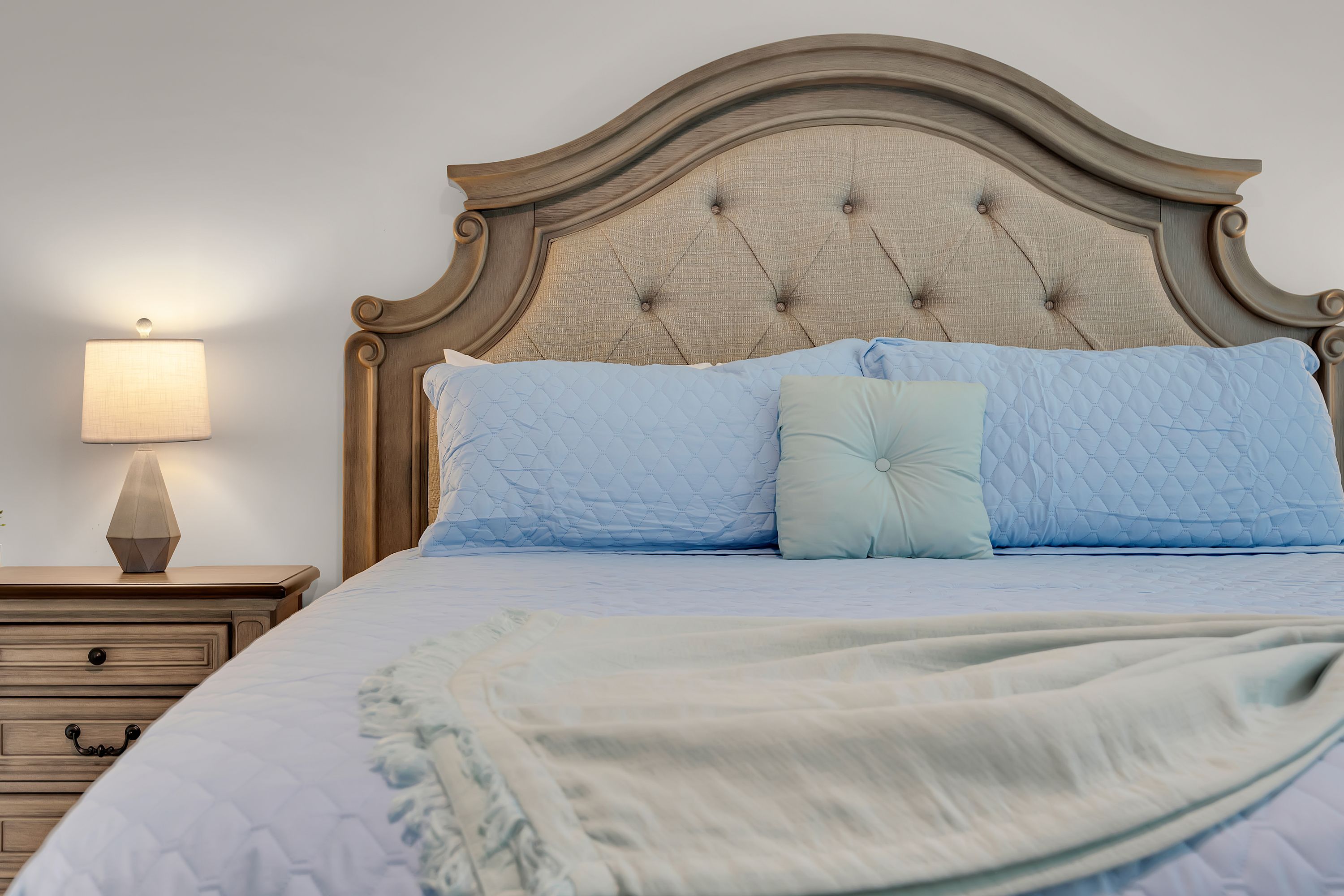 Un lit avec une tête de lit, une table de chevet avec une lampe et une commode.