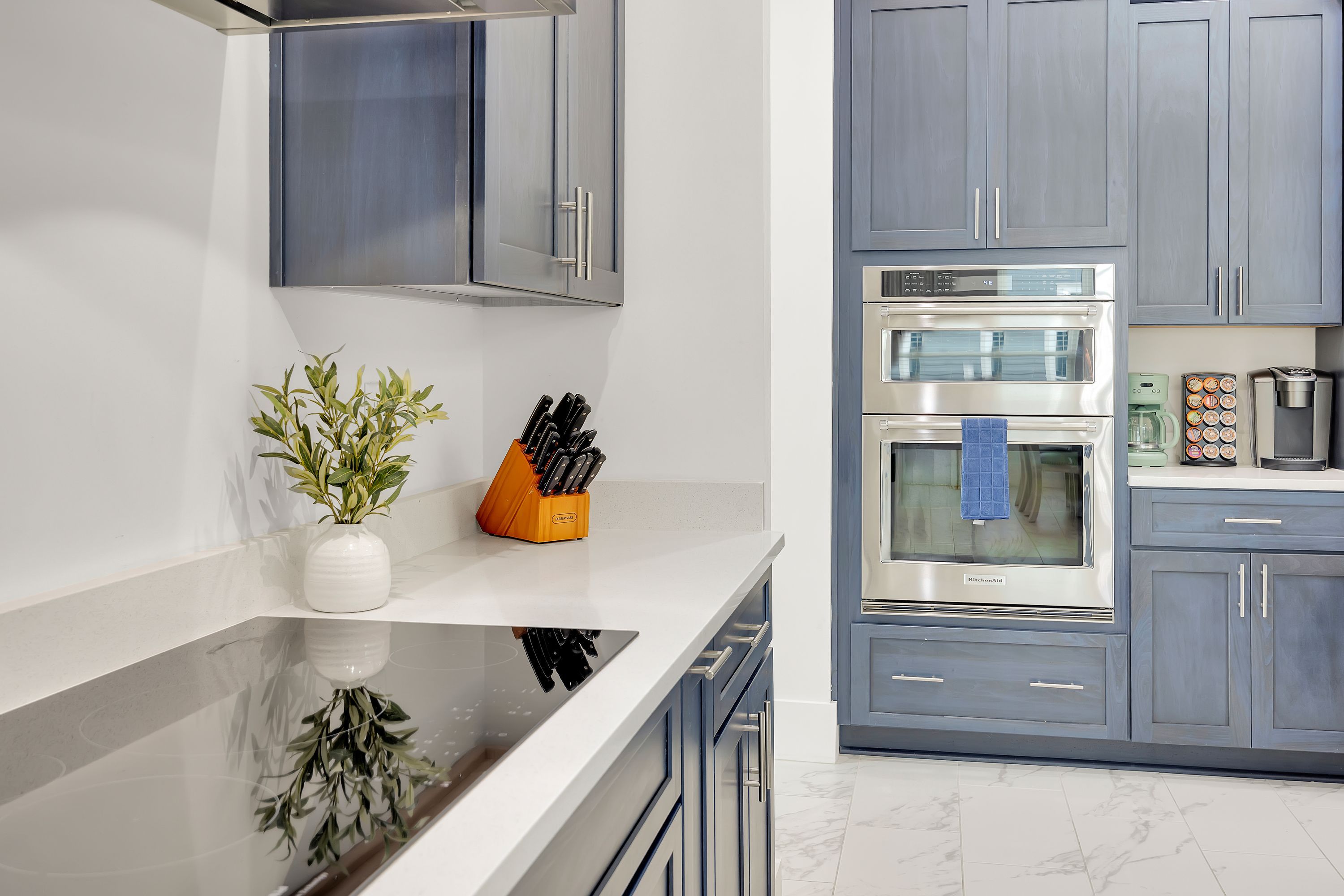 A modern kitchen with stainless steel appliances, a white countertop, and grey cabinetry.