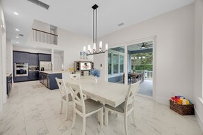 A modern kitchen with dark cabinets, a central island, and a dining area with a white table and chairs.