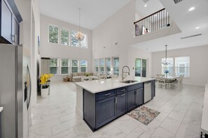 A spacious kitchen with a large island, a dining area, and a living space with a high ceiling and large windows.