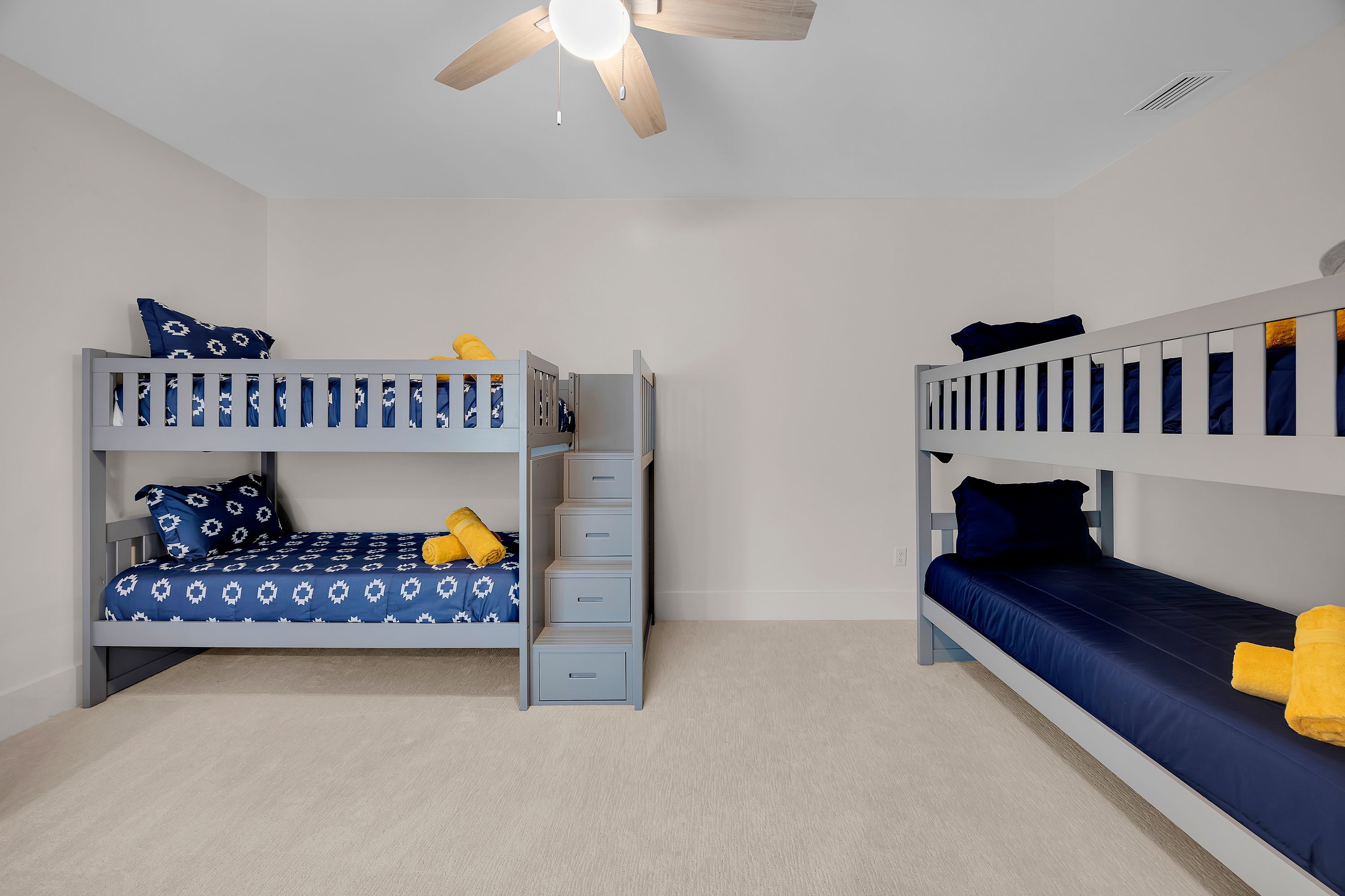 A room with two bunk beds, each with a storage drawer, a ceiling fan, and a light fixture.