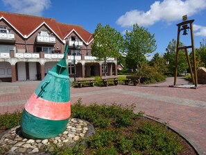 A courtyard with a large sculpture, benches, and a building with a red roof. - Holiday Home in Dornum With Swimming Pool (Dornum)