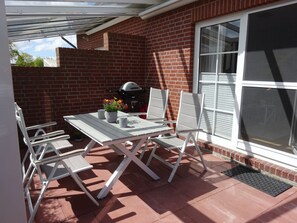 An outdoor patio with a white table and chairs, a grill, and a window. - Holiday Home in Dornum With Swimming Pool (Dornum)