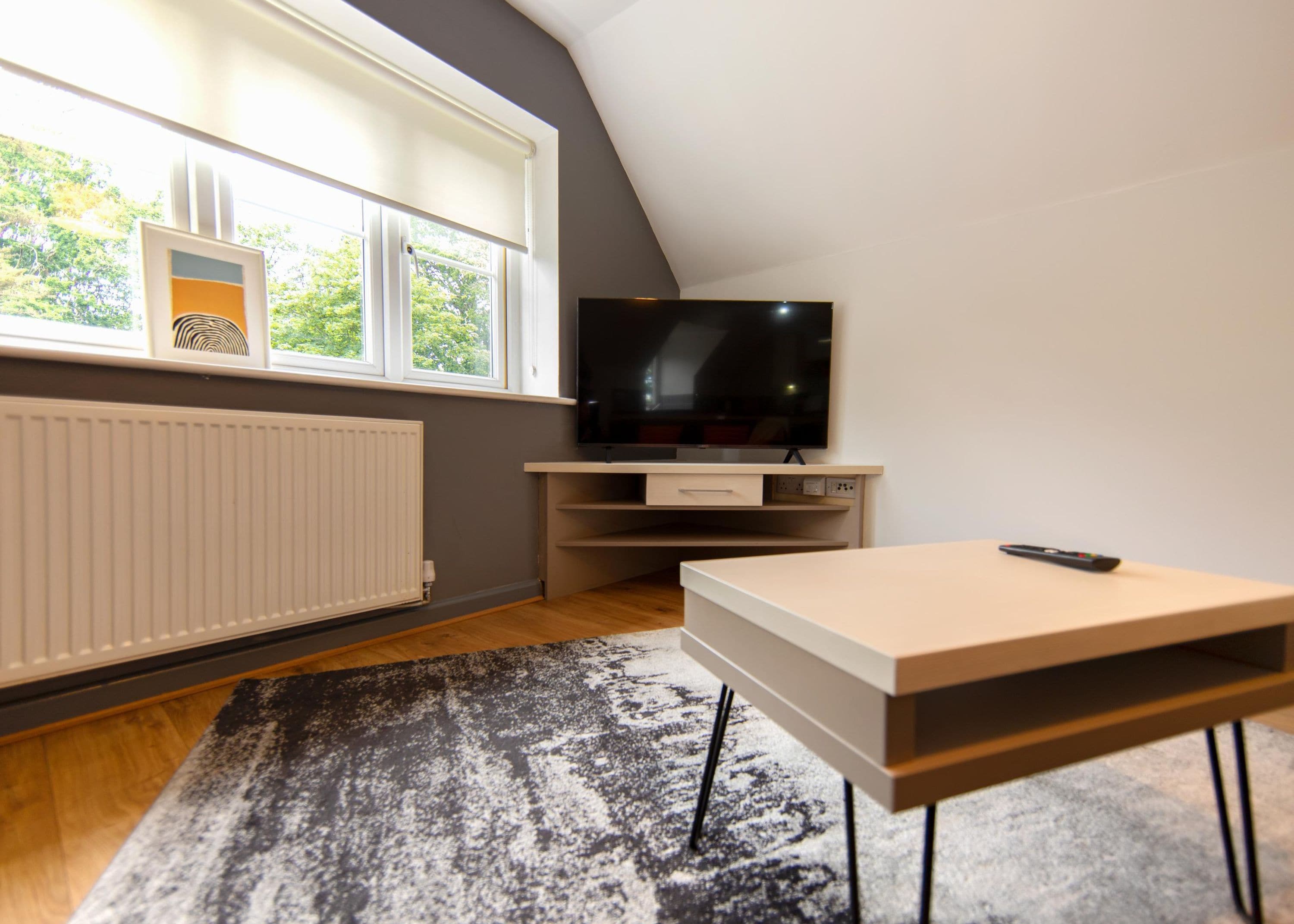 A modern living room with a flat-screen TV, a wooden table, and a window with blinds.