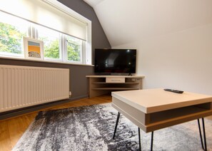 Una sala de estar moderna con un televisor de pantalla plana, una mesa de madera y una ventana con persianas.