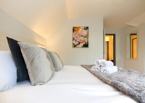 A hotel room with a bed, pillows, a painting, and a rolled towel on the side. - New 1 Bedroom Apartment With Free Parking (Southampton)