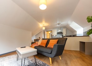 A modern living room with a sofa, a coffee table, and a kitchen in the background. - New 1 Bedroom Apartment With Free Parking (Southampton)