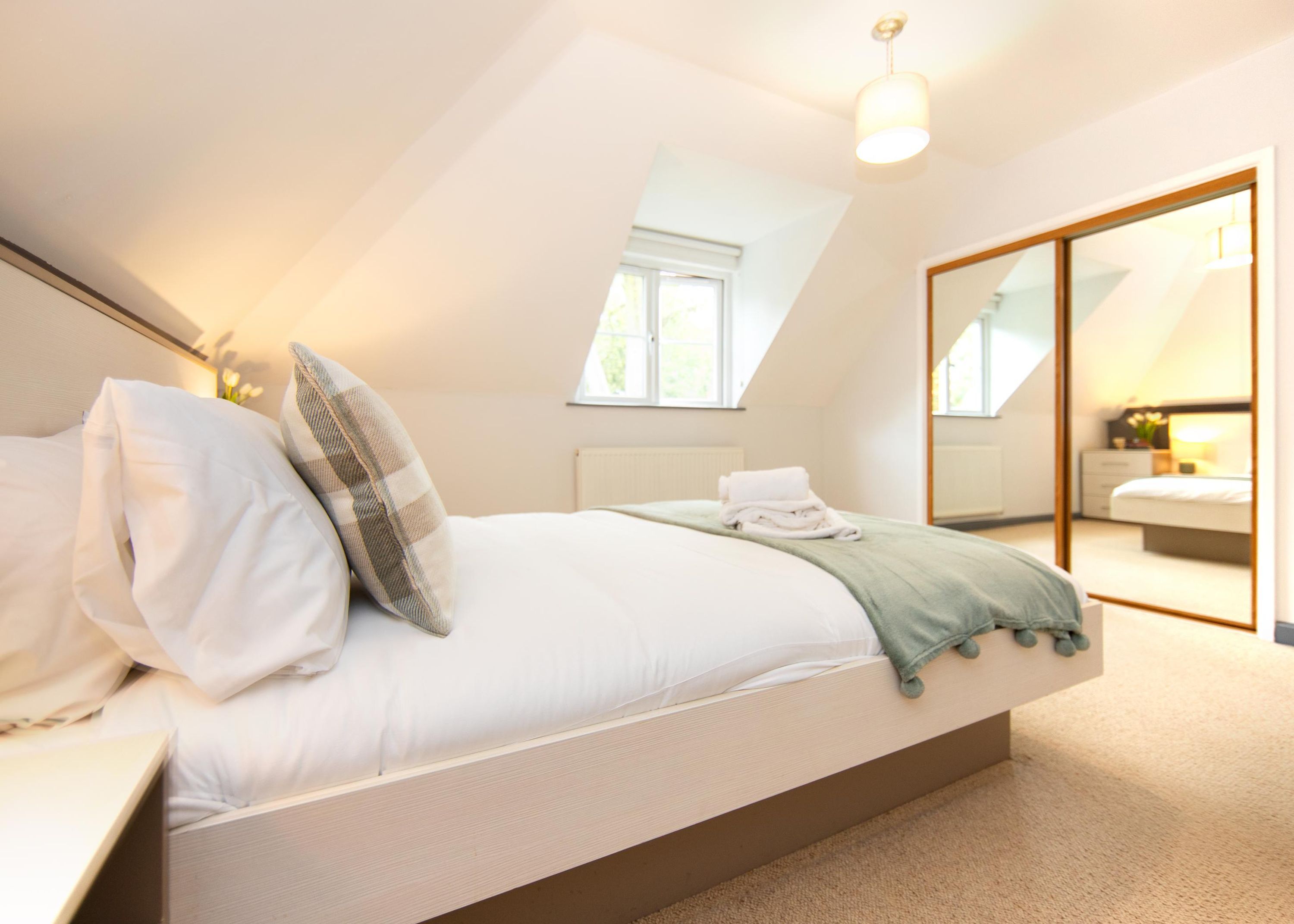 A bedroom with a large bed, a mirror, and a view of another room.