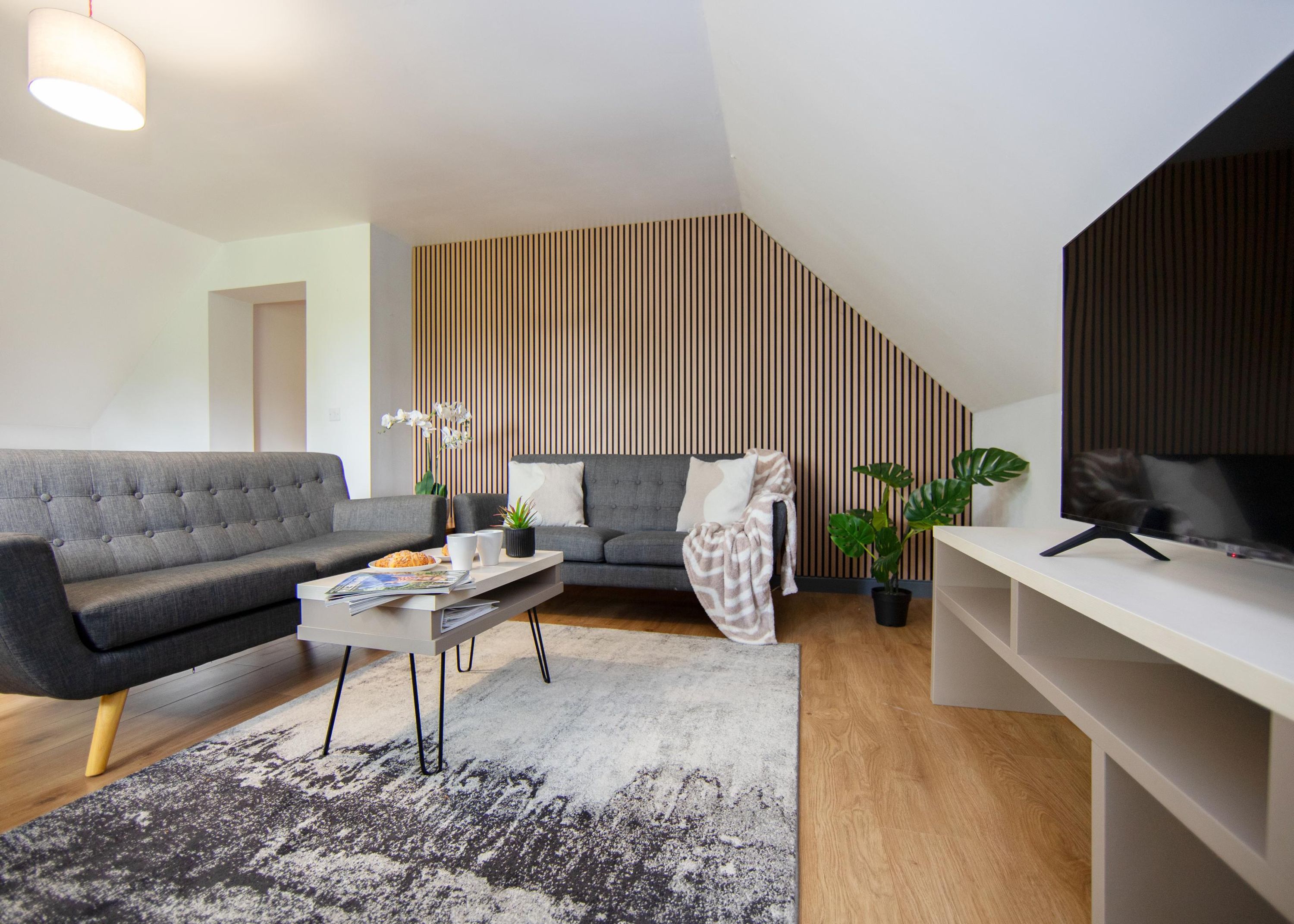 A modern living room with a grey sofa, a coffee table, a TV, and a striped wall.