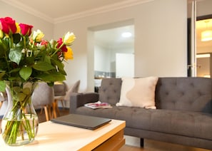 A living room with a grey sofa, a wooden coffee table, and a vase with flowers. - Newly Refurbished 3 Bed Apartment Free Parking (Southampton)