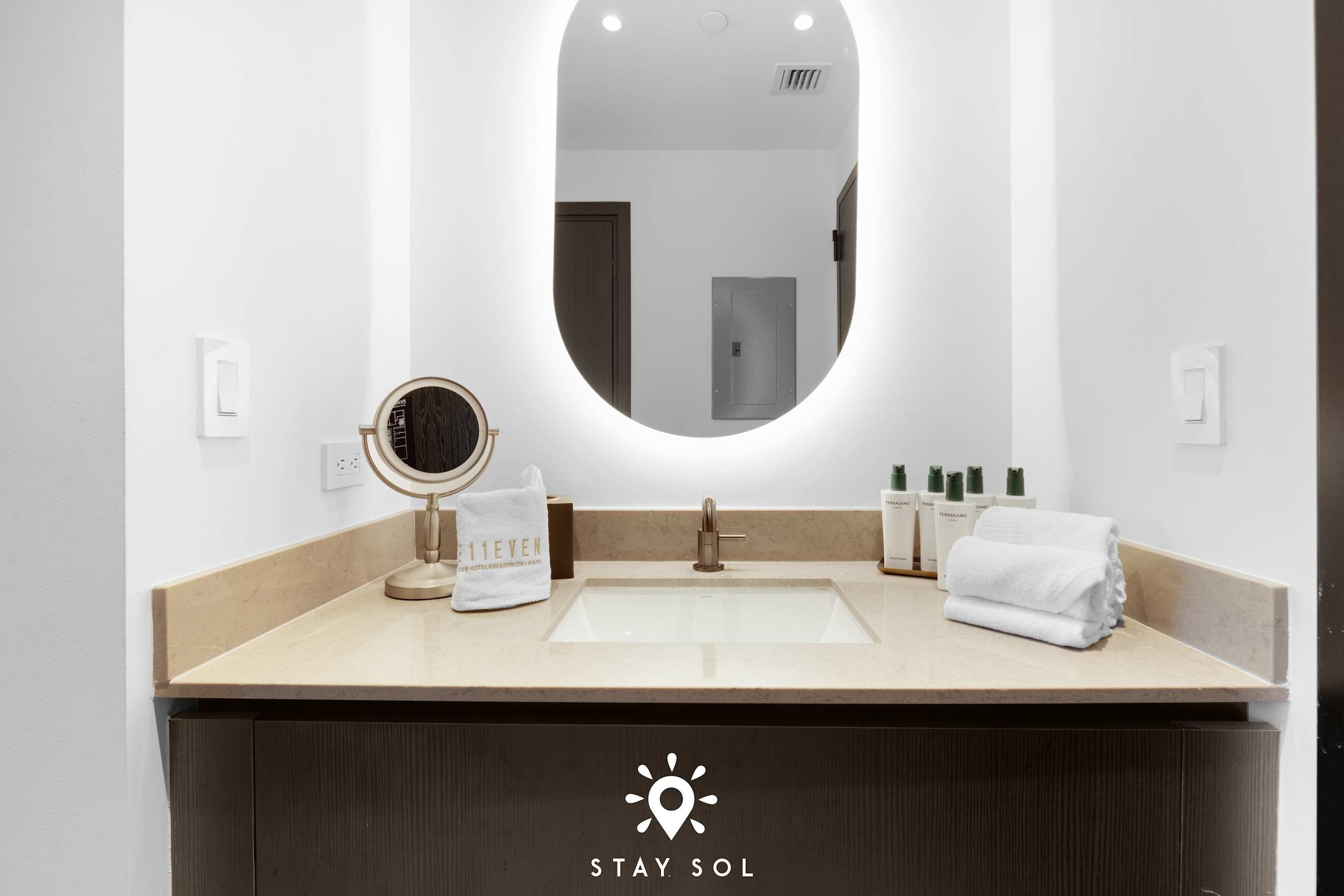 A modern bathroom with a large mirror, a round vanity mirror, and a sink. There are toiletries and a towel on the counter.