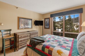 A bedroom with a large window, a wooden dresser, a bed with a quilt, and two framed pictures on the wall. - Skycrest 1721 - Big Sky (Big Sky)