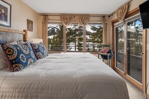 Ein Schlafzimmer mit einem großen Bett, einem Sessel, einem Fernseher und Blick auf eine verschneite Berglandschaft.