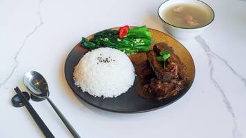 A plate with white rice, a meat dish, green vegetables, and a soup cup on a marble table.
