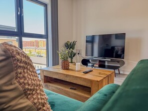 Una sala de estar moderna con un gran ventanal, un televisor de pantalla plana, una mesa de centro de madera y un sofá verde.