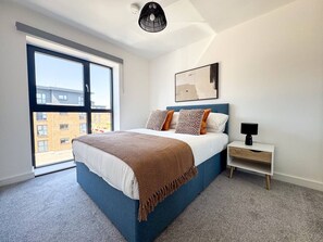 A bedroom with a large bed, a nightstand, a window, and a ceiling light. - Derby City Centre Apt | Free Parking | Long Stays (Derby)