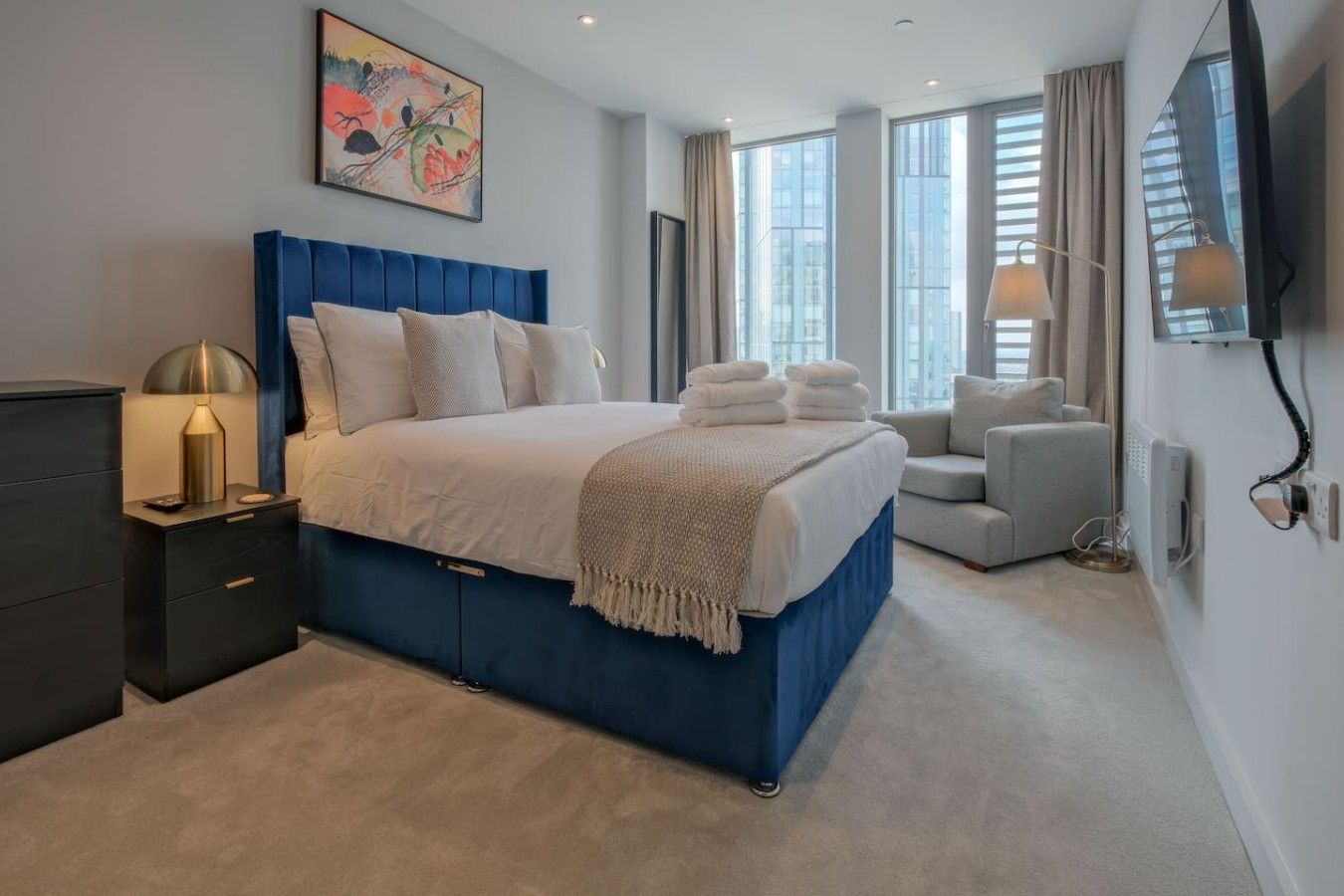 A modern bedroom with a large bed, bedside tables, a TV, and a window with curtains.