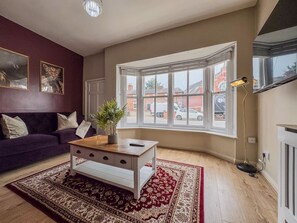 A living room with a sofa, a coffee table, a large window, and a radiator. - Central Stratford Retreat | Town Centre (Warwickshire)
