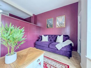 A room with a purple sofa, a wooden coffee table, a potted plant, and a patterned rug. - Central Stratford Retreat | Town Centre (Warwickshire)