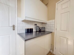 A compact kitchen with white cabinetry, a black countertop, and a kettle. - Central Stratford Retreat | Town Centre (Warwickshire)