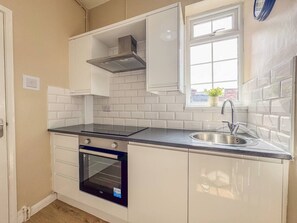 A compact kitchen with white cabinetry, a built-in oven, a stainless steel sink, and a window above the sink. - Central Stratford Retreat | Town Centre (Warwickshire)