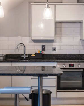 A modern kitchen with white cabinets, a black countertop, a stainless steel sink, and a built-in oven. - Central 1 Bed | Prime Stratford Town Centre (Stratford-upon-Avon)