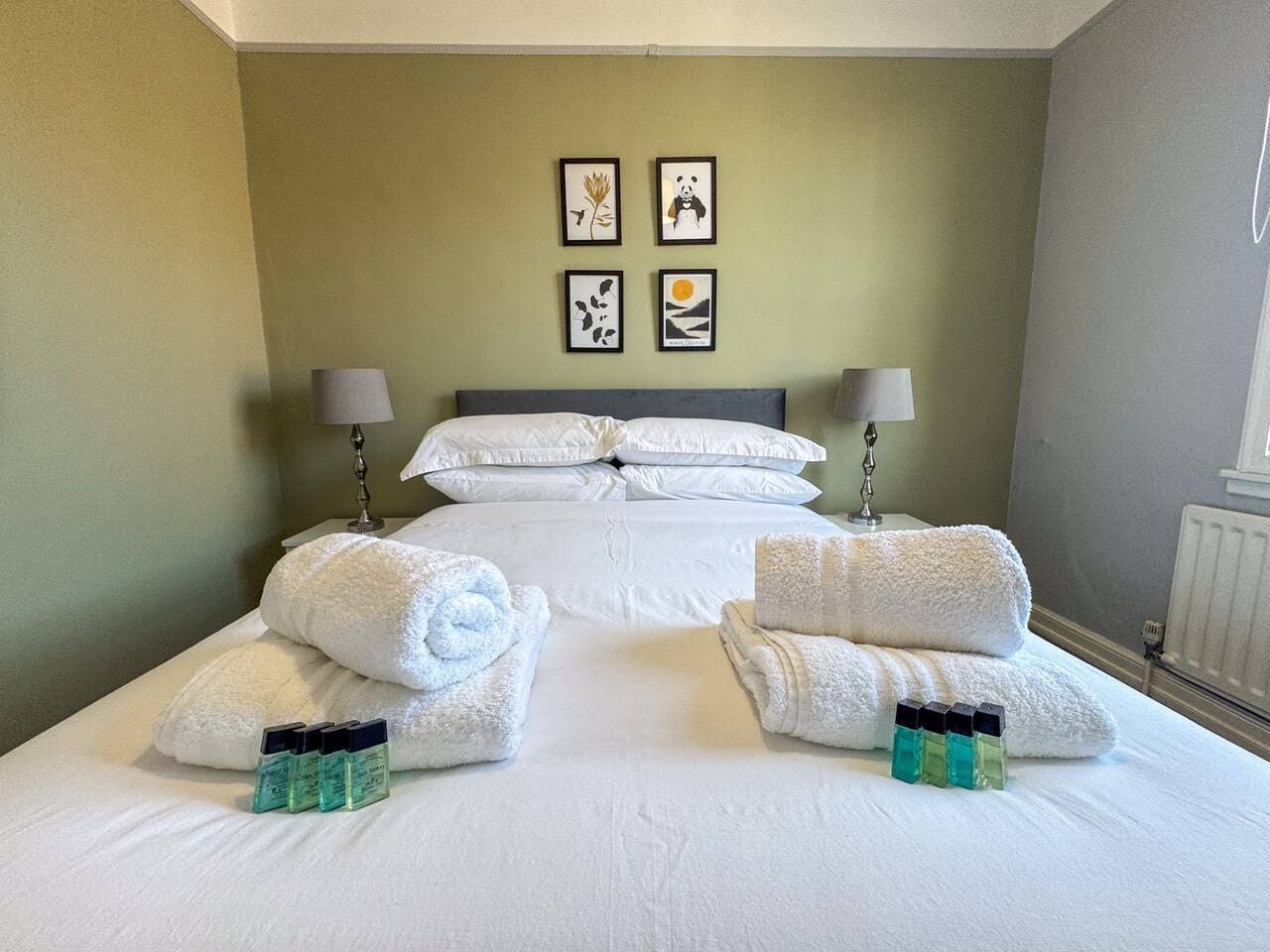 A hotel room with a large bed, two bedside tables with lamps, a radiator, and artwork on the wall.