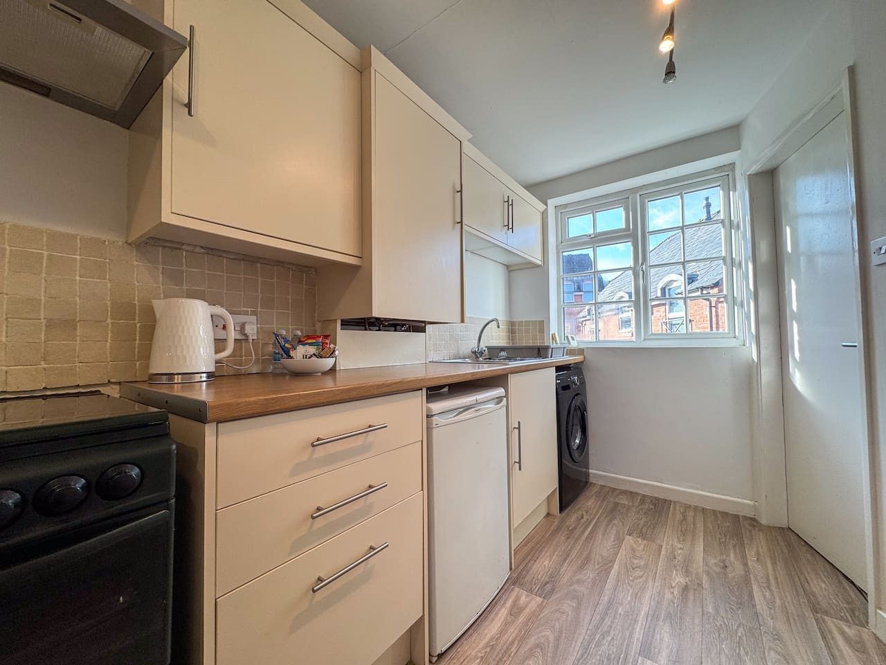 A compact kitchen with a stove, dishwasher, and a window providing a view of the outside.