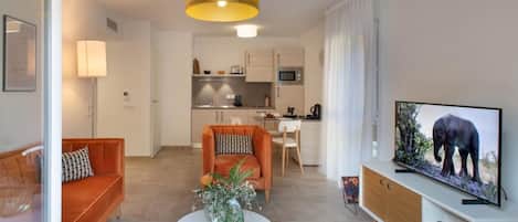 Una sala de estar moderna con un sofá, una mesa de centro con un florero, un televisor y una cocina al fondo.