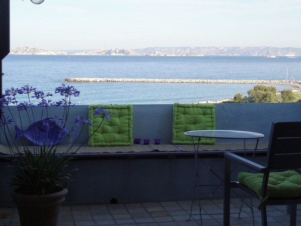 Un balcó amb vista al mar, una cadira, una taula petita i una planta en test.