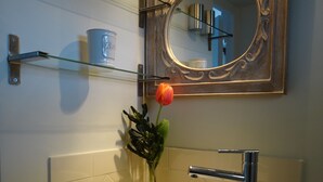 Ein Badezimmer mit einem weißen Waschbecken, einem Spiegel und einer Glasablage für Toilettenartikel.