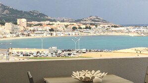 Eine Küstenstadt mit Strand, geparkten Autos und einem Berg im Hintergrund.