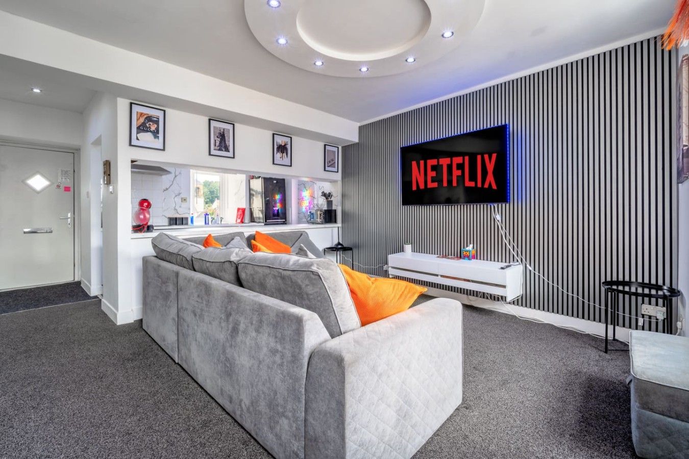 Un salon moderne avec un canapé gris, un téléviseur à écran plat affichant le logo « NETFLIX » et un meuble de rangement blanc.