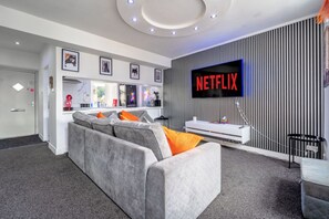 Un salon moderne avec un canapé gris, un téléviseur à écran plat affichant le logo « NETFLIX » et un meuble de rangement blanc.