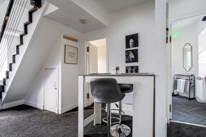 Un intérieur moderne avec un escalier, un coin bar et une salle de bain visible à travers une porte ouverte.