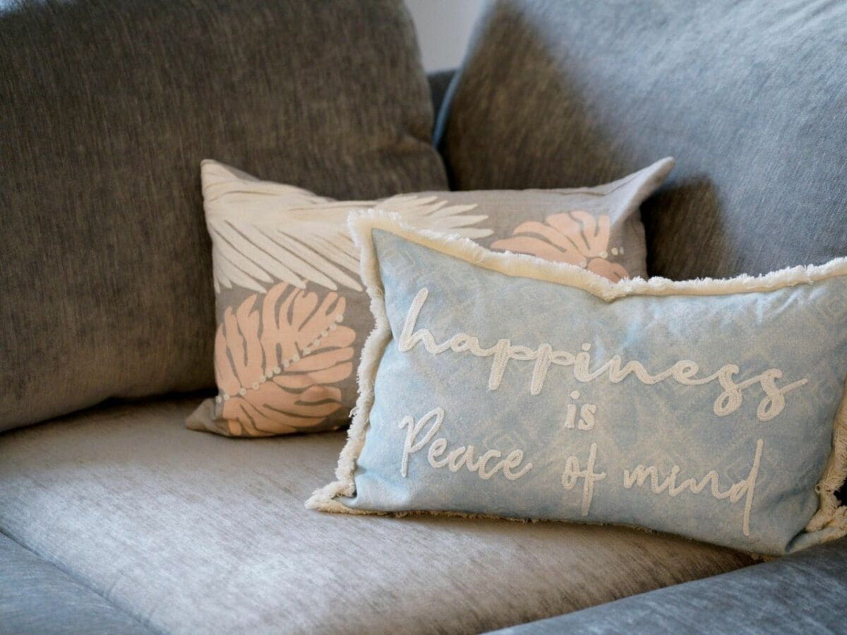 Un sofá gris con dos almohadones decorativos, uno con estampado floral y el otro con bordado.