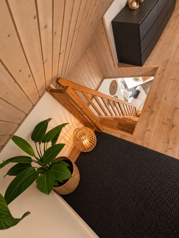 A wooden staircase leading to a room with a black cabinet, a white sofa, and a small table with a plant.