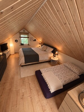 Une chambre mansardée chaleureuse avec un plafond en pente, un lit, une table de chevet, une lampe et un téléviseur.