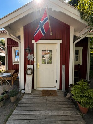 A wooden house with a white door, a red flag, and a doormat.