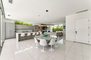 A modern kitchen with a central island, white bar stools, and a dining table with white chairs. - Peaks & Palms Modern home,  exceptional views. High end everything! Lic #069416 (Palm Springs)