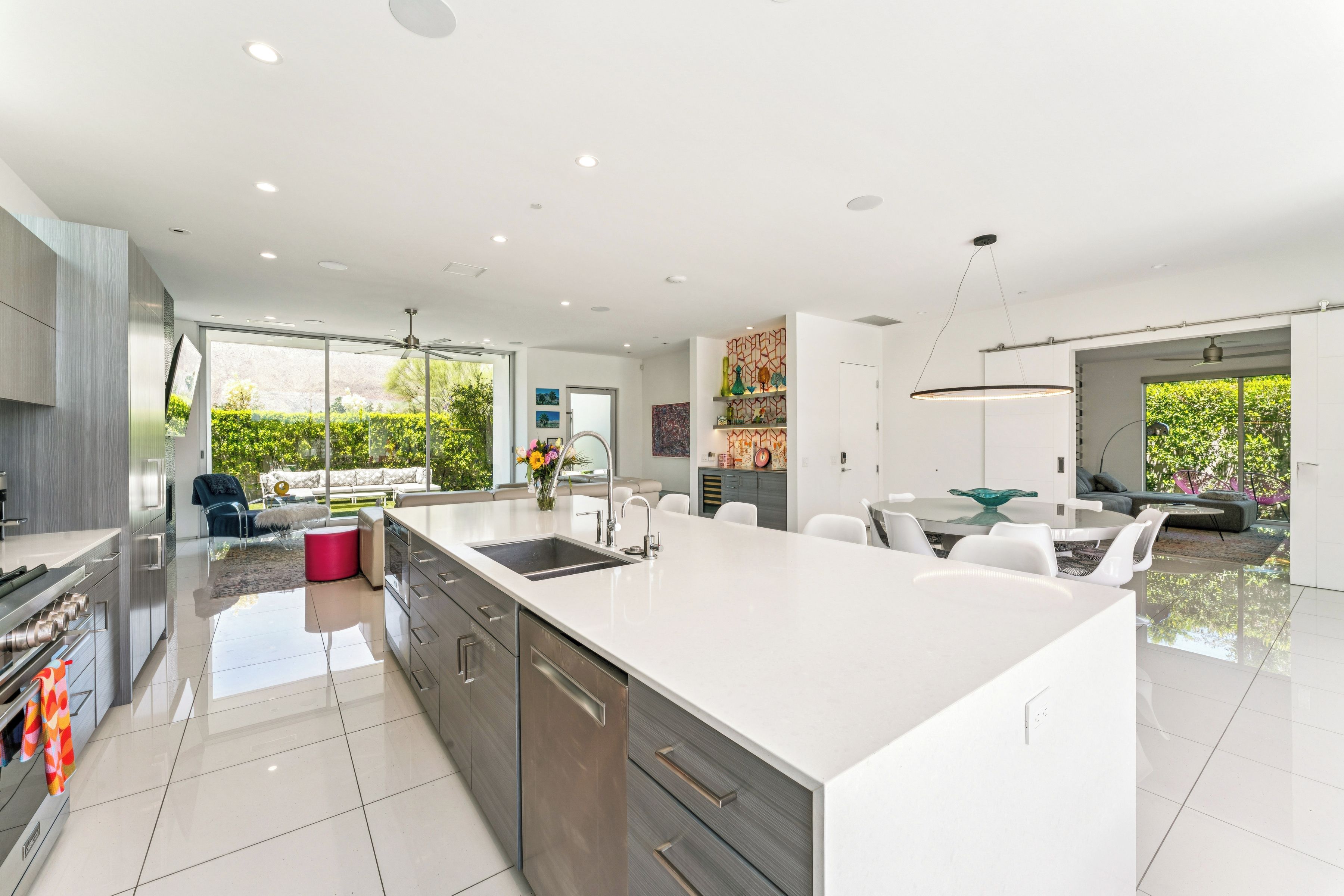 A modern kitchen with a large island, stainless steel appliances, and a dining area with a glass table and white chairs.