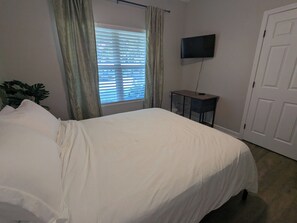 A bedroom with a bed, a television mounted on the wall, a window with curtains, and a door. - Private 3-bedroom house with Hot Tub near White Water Center and Belmont (Mount Holly)