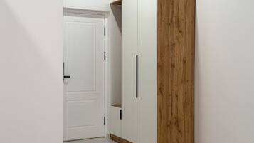 A wardrobe with a wooden finish and two doors, located in a hallway with a white door in the background.