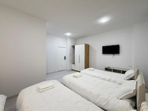 A hotel room with two beds, a wardrobe, a television, and a door. - CMC HOTEL (Samarkand)