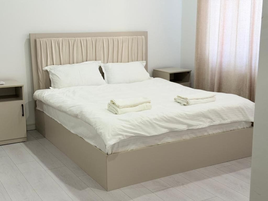 Una cama con cabecera, dos almohadas, una mesita de noche y una toalla doblada sobre la cama.